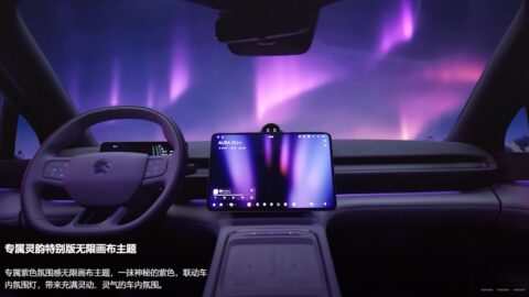 Interior view of the Nio EC6 Aura Edition from the driver's seat, with the central infotainment screen displaying the purple Aura Glow theme and purple aurora-like lighting shown through the windshield.