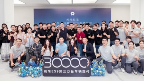 Attendees give thumbs-up gestures behind a sign celebrating the delivery of Nio's 30,000th ES9.