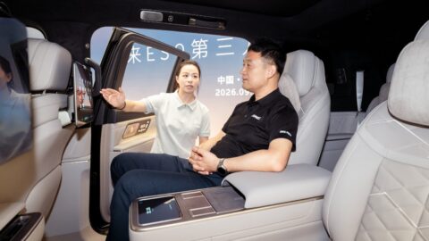 Insnex chairman He Yinjun sits in a Nio ES9's second-row seat as a staff member demonstrates the rear passenger screen.