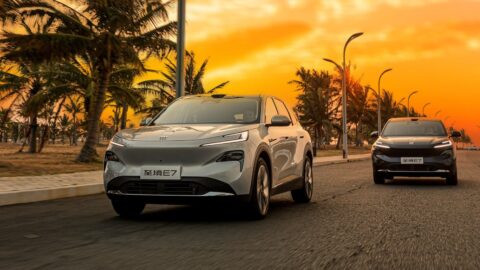2 Buick Electra E7 plug-in hybrid SUVs driving along a palm-lined road at sunset.