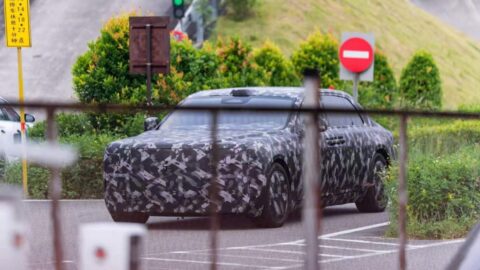 Front three-quarter view of a camouflaged Yangwang executive sedan prototype, partially obscured by a fence.