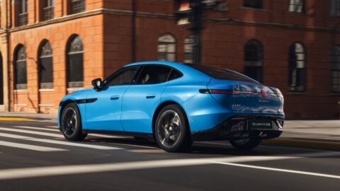 Rear three-quarter view of a blue Volkswagen ID. UNYX 09 on a city street beside a red-brick building.