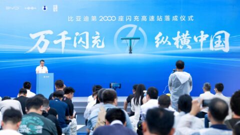 A speaker addresses an audience at a podium in front of a blue backdrop celebrating BYD’s milestone of 2,000 highway flash-charging stations.