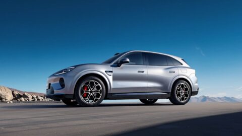 Silver Aistaland GX7 SUV shown from a front three-quarter angle on a paved road with mountains in the background.