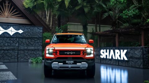 Front view of an orange BYD Shark pickup with illuminated headlights beside a Shark sign.