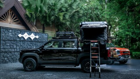 Black BYD Shark pickup equipped with a roof rack and a deployed tent above the cargo bed, accessed by a ladder.