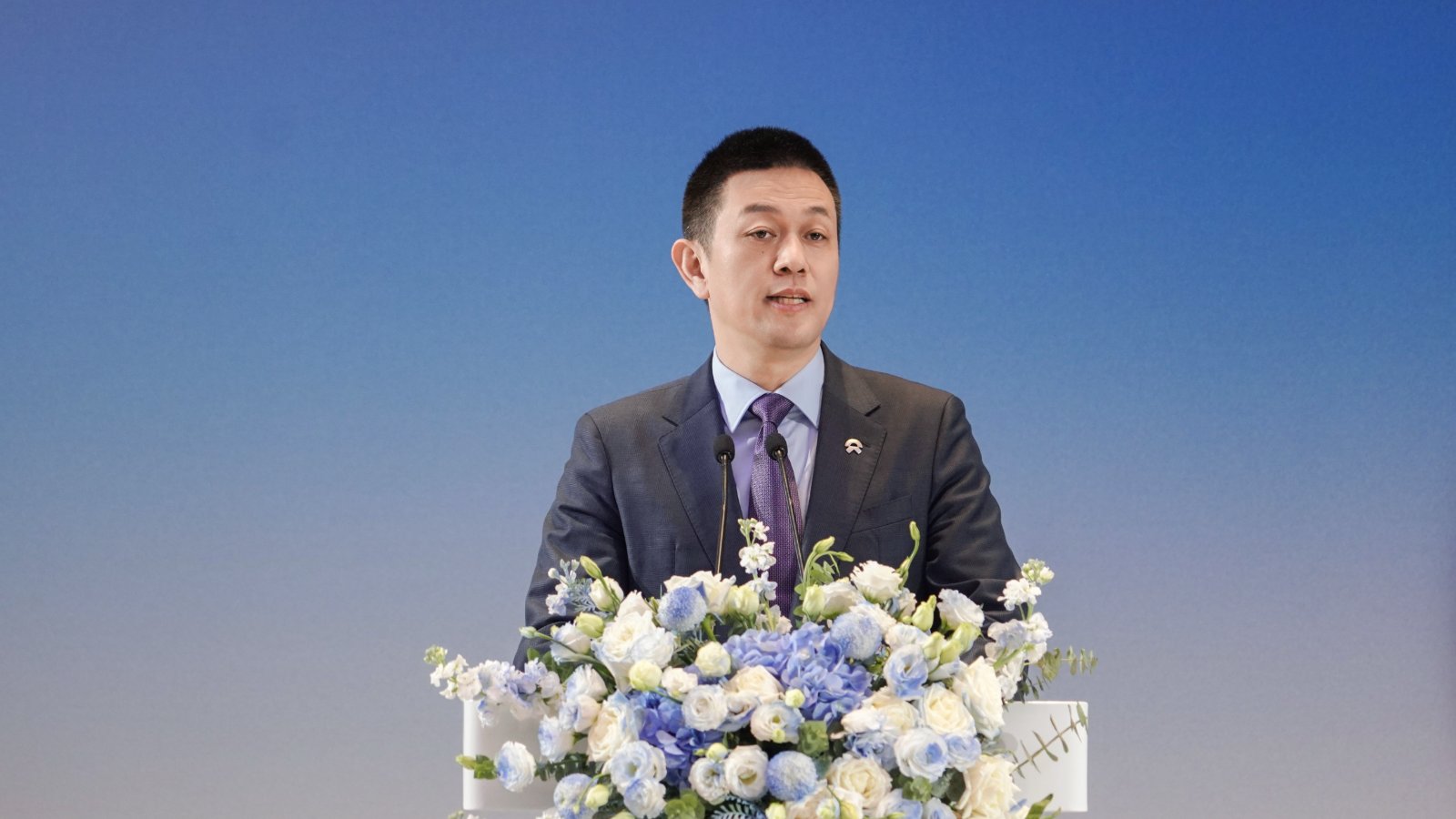 Nio founder William Li speaks at a flower-adorned podium during the Geely-Nio partnership event.