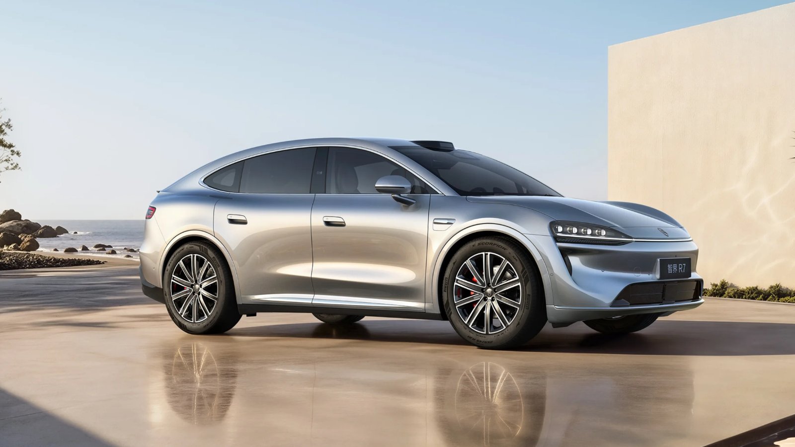 Silver Luxeed R7 coupe SUV shown from a front three-quarter angle beside the sea.