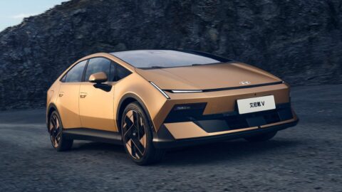 Gold Hyundai Ioniq V viewed from the front three-quarter angle against a rocky backdrop.