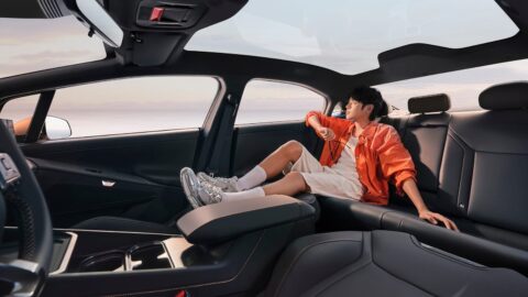 Passenger relaxing in a Hyundai Ioniq V with the front seat folded flat beneath the panoramic glass roof.