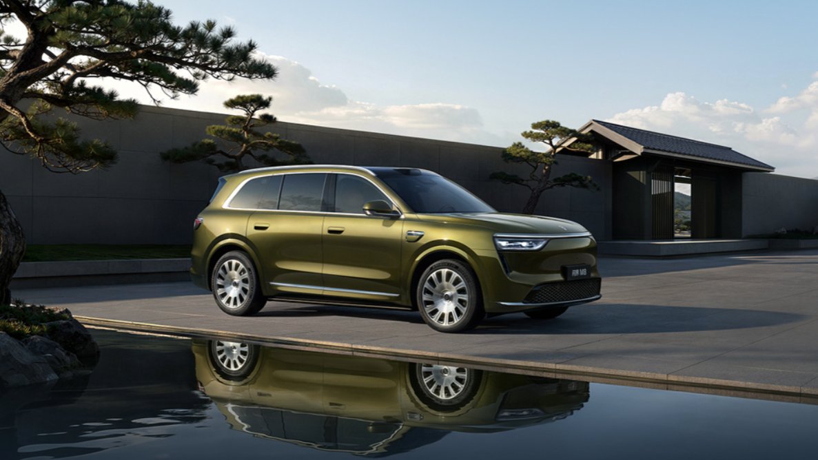 Front three-quarter view of a green updated Aito M8 SUV beside a reflecting pool in a landscaped courtyard.