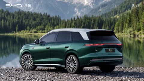 Rear three-quarter view of a green third-generation BYD Tang with a silver roof beside a mountain lake.