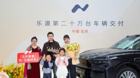 A family poses with flowers beside an Onvo L90 at the brand's 200,000th vehicle delivery ceremony in Beijing.