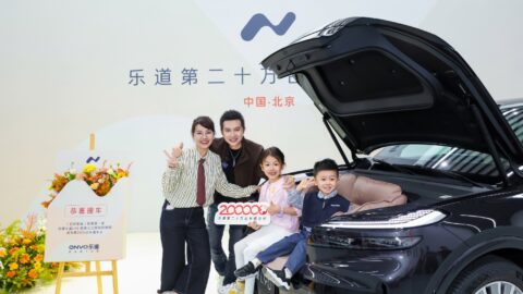 A family poses beside an Onvo L90 with its hood open and 2 children sitting in the spacious front trunk.