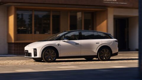 A side profile of the 2026 Li i6 in white, driving along a cobblestone street past a coffee roasting shop with large wooden-framed windows.