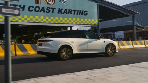 A rear three-quarter view of the 2026 Li i6 in white, driving past a go-kart track with a "North Coast Karting" sign and yellow-and-black striped barriers.