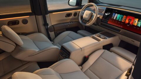 The front cabin of the 2026 Li i6 with cream leather seats, a two-tone steering wheel, a wide curved infotainment display, warm ambient lighting and a center console with cupholders. The front passenger seat is reclined with a pillow-style headrest.