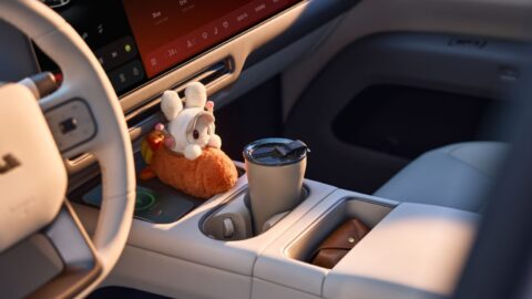 A close-up of the 2026 Li i6's center console, showing a wireless charging pad with a plush toy on it, a tumbler in the cupholder and a brown leather pouch in the storage tray, with the steering wheel and infotainment screen in the background.