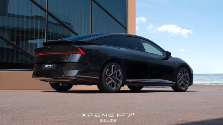 Rear three-quarter view of a black Xpeng P7+ Black Knight edition parked by the sea, showing its full-width red light bar, ducktail spoiler, blacked-out badging and dark machine-faced wheels.