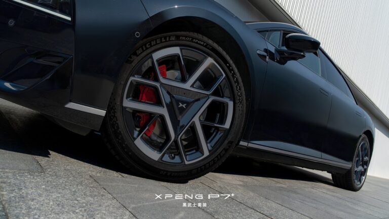 Low-angle close-up of the Xpeng P7+ Black Knight edition's front wheel, showing a dark multi-spoke alloy design with red brake calipers and Michelin Pilot Sport EV 255/45 R20 tires.