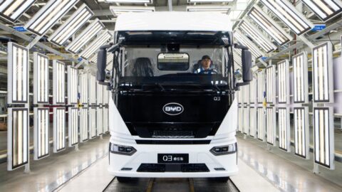 Front view of a white BYD Q3 electric semi-truck inside an illuminated vehicle inspection area.