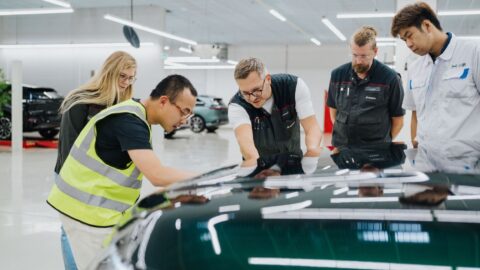 Staff examine the bodywork of a dark green Xpeng G9L inside a factory.