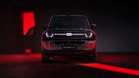 Front view of a dark Geely Galaxy Cruiser 700 with illuminated headlights under red studio lighting.