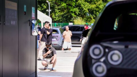 Visitors watch beside a Nio battery swap station, with the rear of an electric hatchback in the foreground.