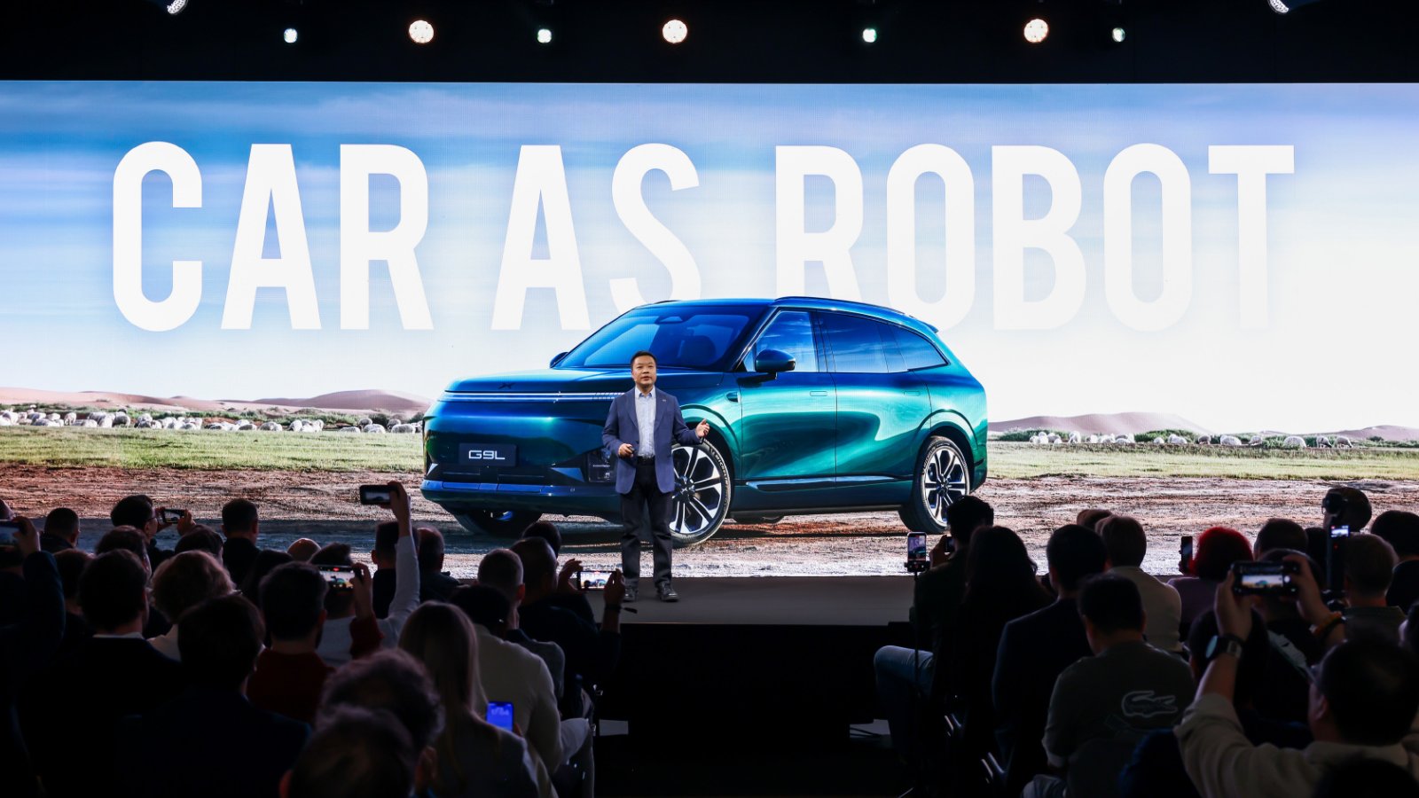 Xpeng chairman and CEO He Xiaopeng speaks onstage in front of a large image of the G9L SUV at the Paris auto show.