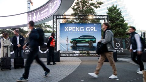Visitors walk past an Xpeng G9L promotional display outside the Paris auto show.