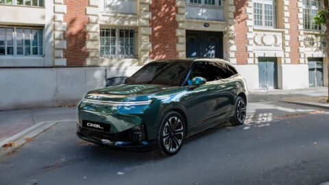 Green Xpeng G9L SUV parked on a cobblestone street outside a brick and stone building.
