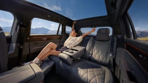 A passenger reclines in the Volkswagen ID. ERA 8X's rear cabin beneath a panoramic glass roof, with the center armrest lowered.