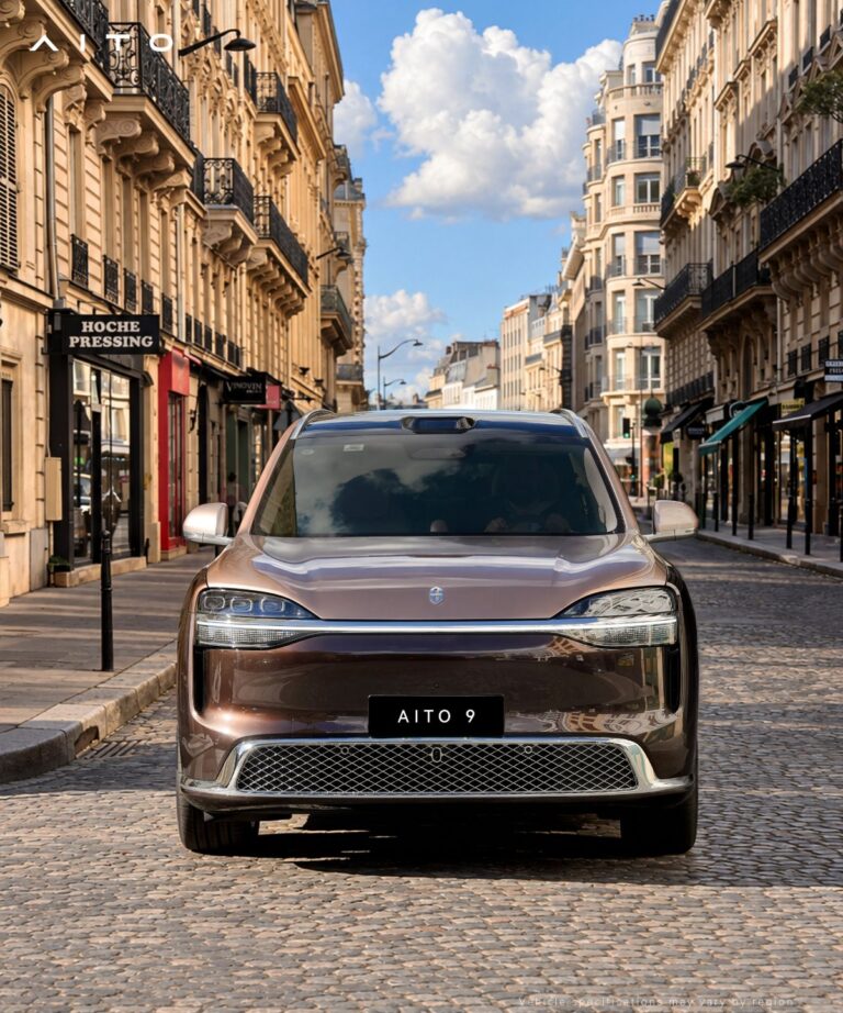 Front view of a brown Aito 9 SUV on a cobblestone street lined with buildings.