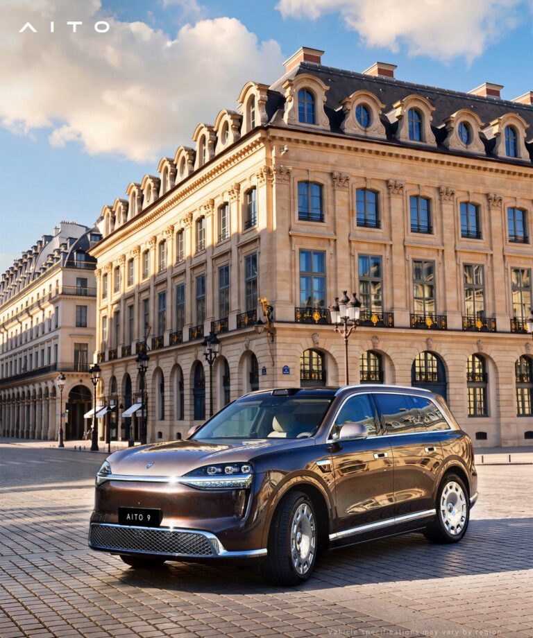 Brown Aito 9 SUV viewed from the front three-quarter angle in a square bordered by ornate stone buildings.