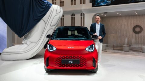 A man standing beside a red Smart #2 at its world premiere.