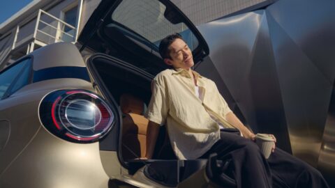 A man sitting on the lowered rear tailgate of a Smart #2 with the upper glass hatch open.