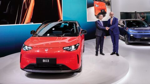 Zhu Jiangming, founder of Leapmotor, and Danilo Annese, CEO of Leapmotor International, shake hands beside a red Leapmotor hatchback at the Paris Motor Show.