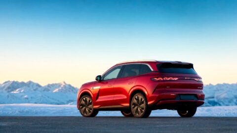 Rear three-quarter view of a red BYD Atto 8 parked beside snow-covered mountains.