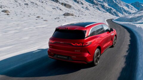 Red BYD Atto 8 driving along a winding road through snow-covered mountains, viewed from behind.