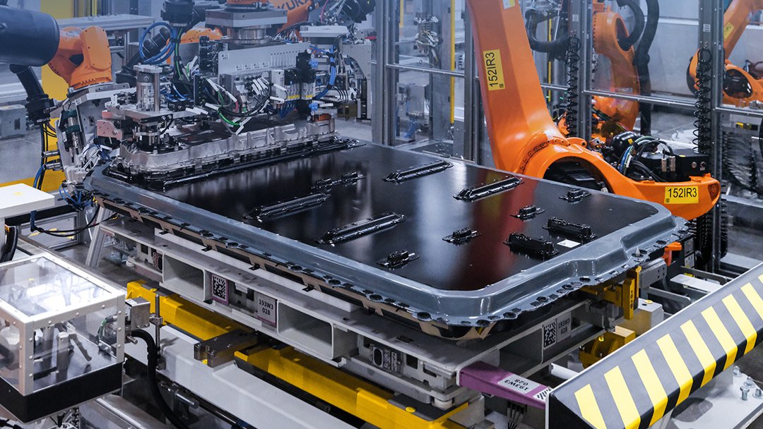 Robotic equipment surrounds a BMW battery pack on an automated assembly line.