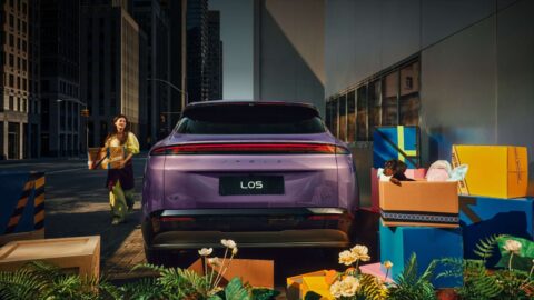 Rear view of a purple Xpeng Mona L05 with a full-width taillight, parked beside colorful outdoor seating.