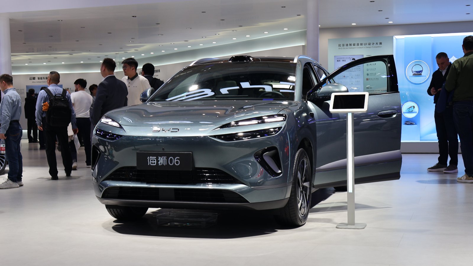 A gray BYD Sealion 06 SUV on display with a front door open and visitors nearby.
