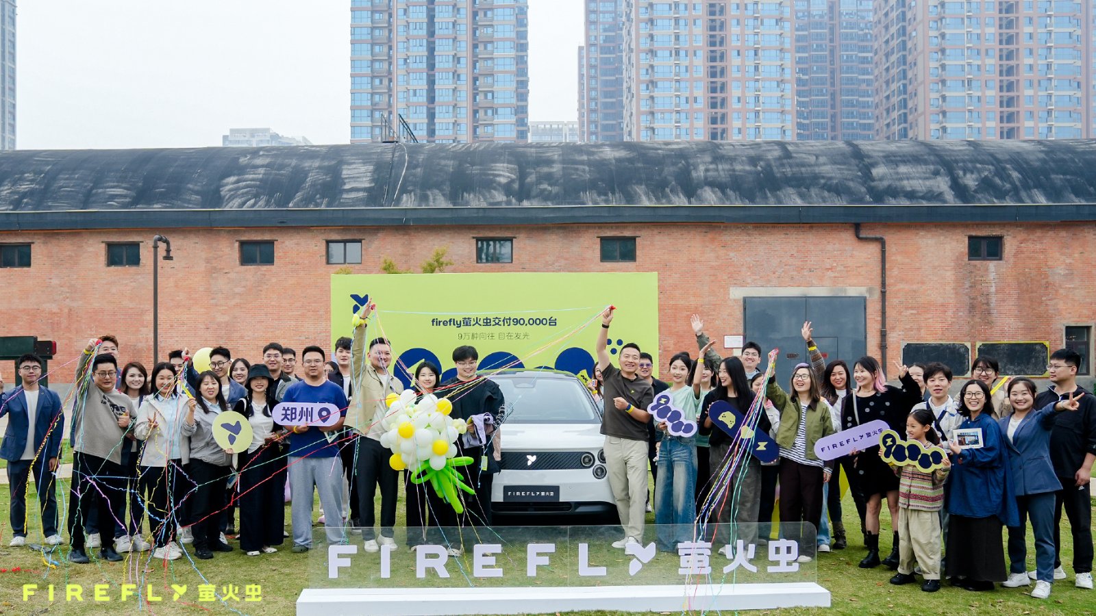 Attendees gather around a white Firefly EV with colorful streamers and signs celebrating 90,000 deliveries.