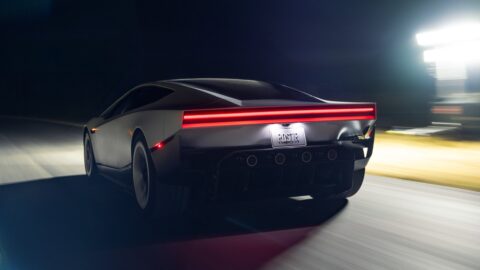 Tesla Roadster driving at night, viewed from the rear with its red taillight illuminated.
