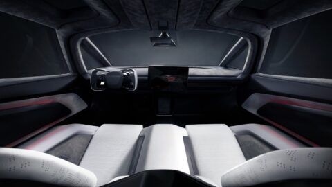 Wide view of the Tesla Roadster cabin, showing white seats, a steering yoke and a broad windshield.