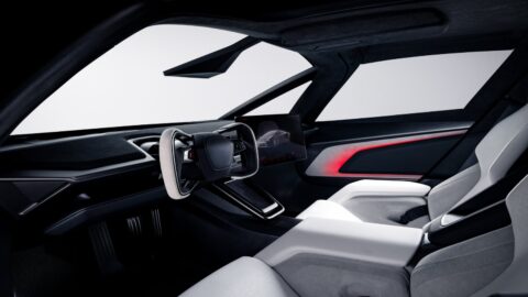 Tesla Roadster interior showing the steering yoke, dashboard, white seats and red door trim.