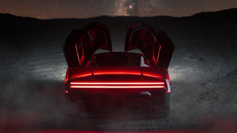 Tesla Roadster viewed from behind at night, with both doors raised and red taillights illuminated.
