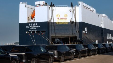 Rows of Xpeng GX SUVs parked in front of a vehicle carrier ship with its loading ramp lowered.