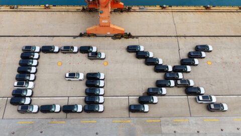 Aerial view of vehicles arranged to spell GX on a dock beside an orange crane.