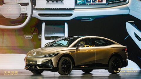 Gold Volkswagen ID. UNYX 07 sedan displayed onstage in front of a large image of its interior.